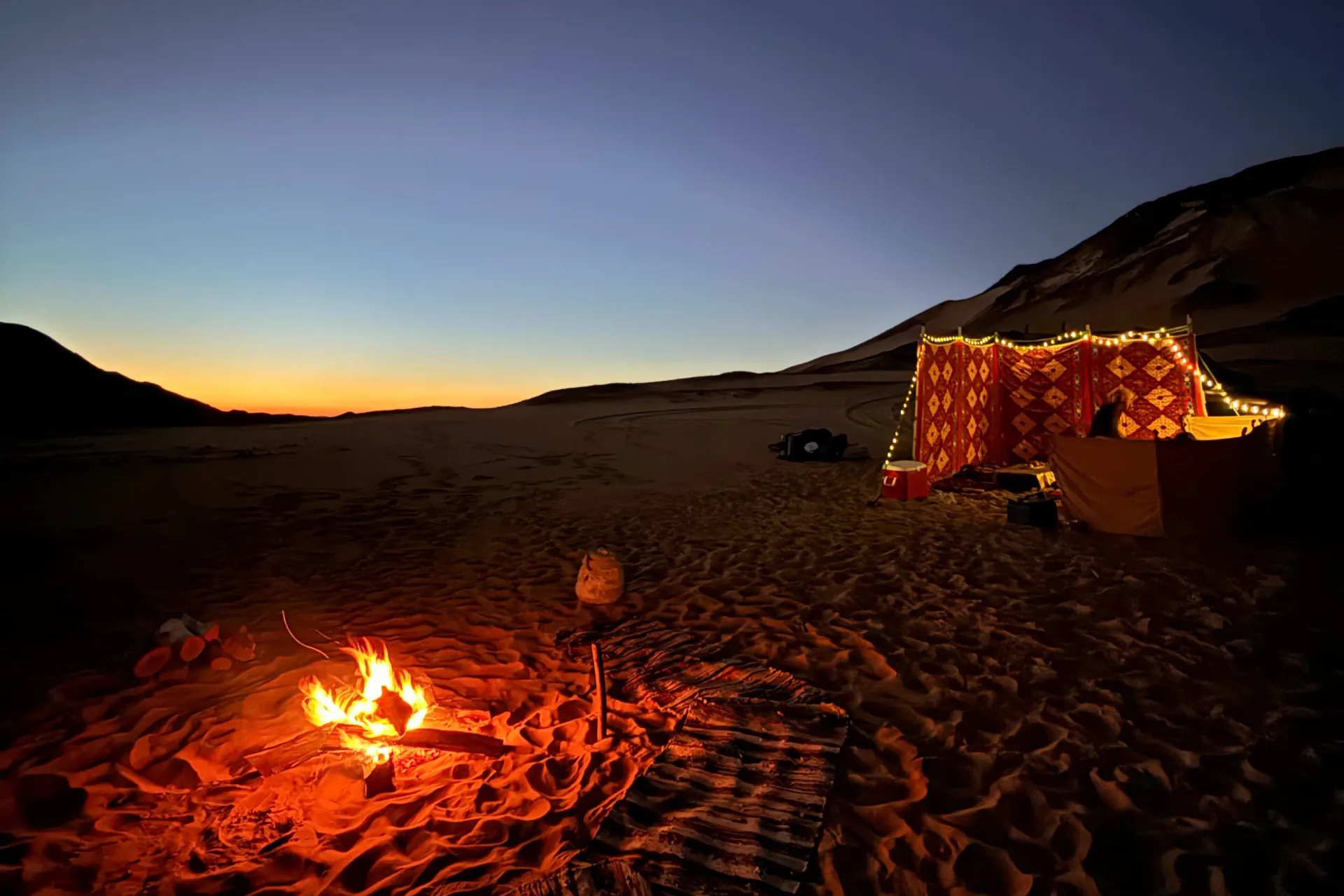 Campfire and illuminated seating at a small-group White Desert camp after sunset
