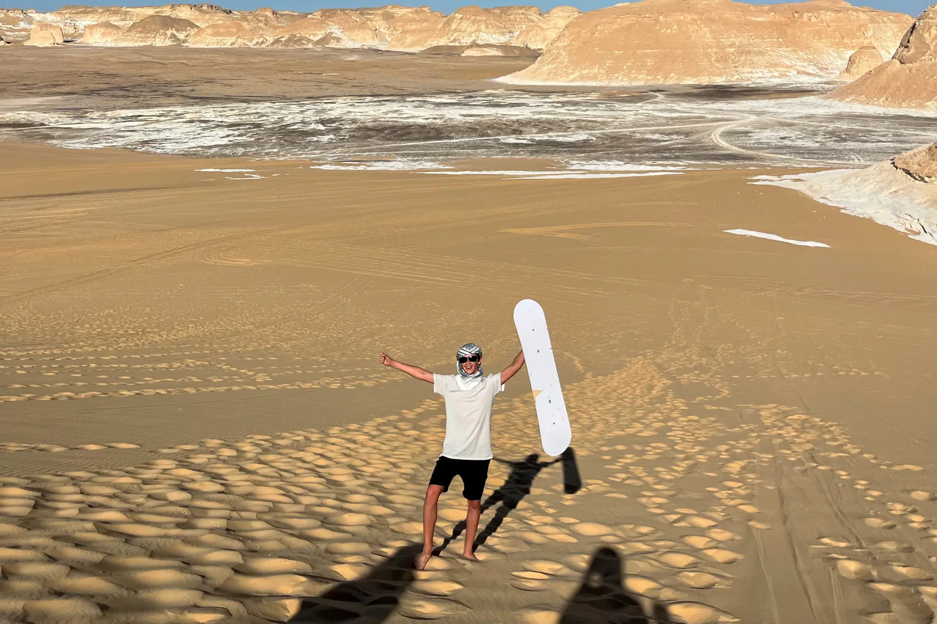 Traveler sandboarding on a high dune during the three day White Desert solar eclipse tour in Egypt